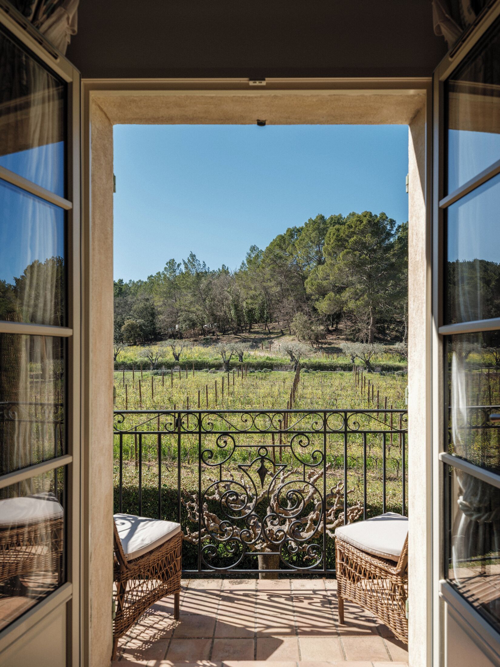 An open balcony with wicker chairs and a wrought iron railing, overlooking a vineyard.
