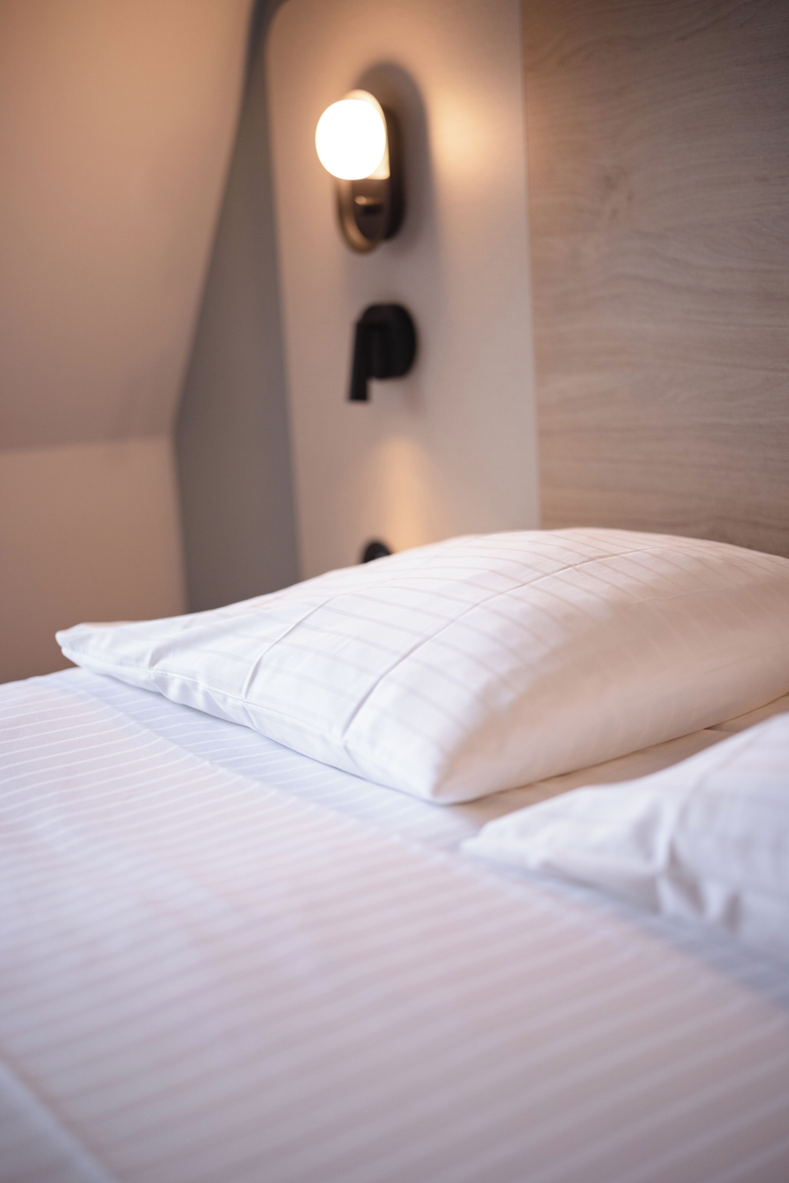 Cama bem arrumada com lençóis brancos e um único travesseiro.