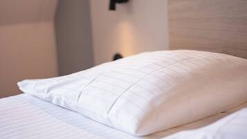 Cama bem arrumada com lençóis brancos e um único travesseiro.