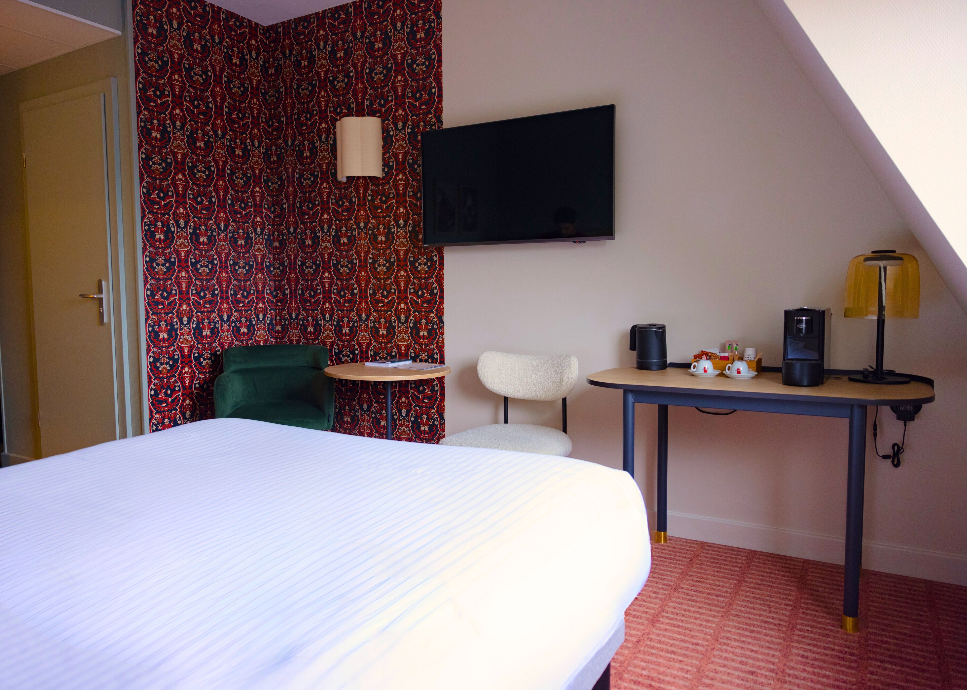 Een hotelkamer met een bed, een bureau met lamp, een stoel, een televisie en een kamer met een patroon op de muur.