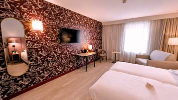 A hotel room with a large bed, a desk, a chair, a TV, and a patterned wall.