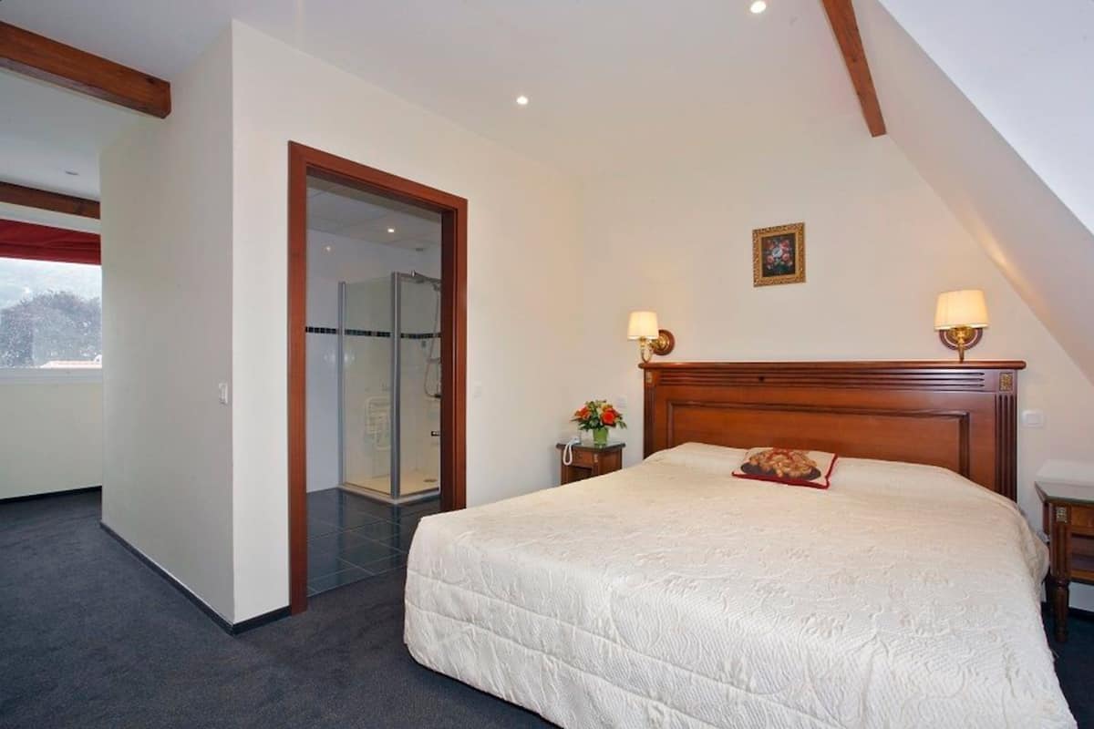 Een slaapkamer met een groot bed, een houten hoofdbord, twee bedlampjes, een kleine tafel met een vaas en een schilderij aan de muur.