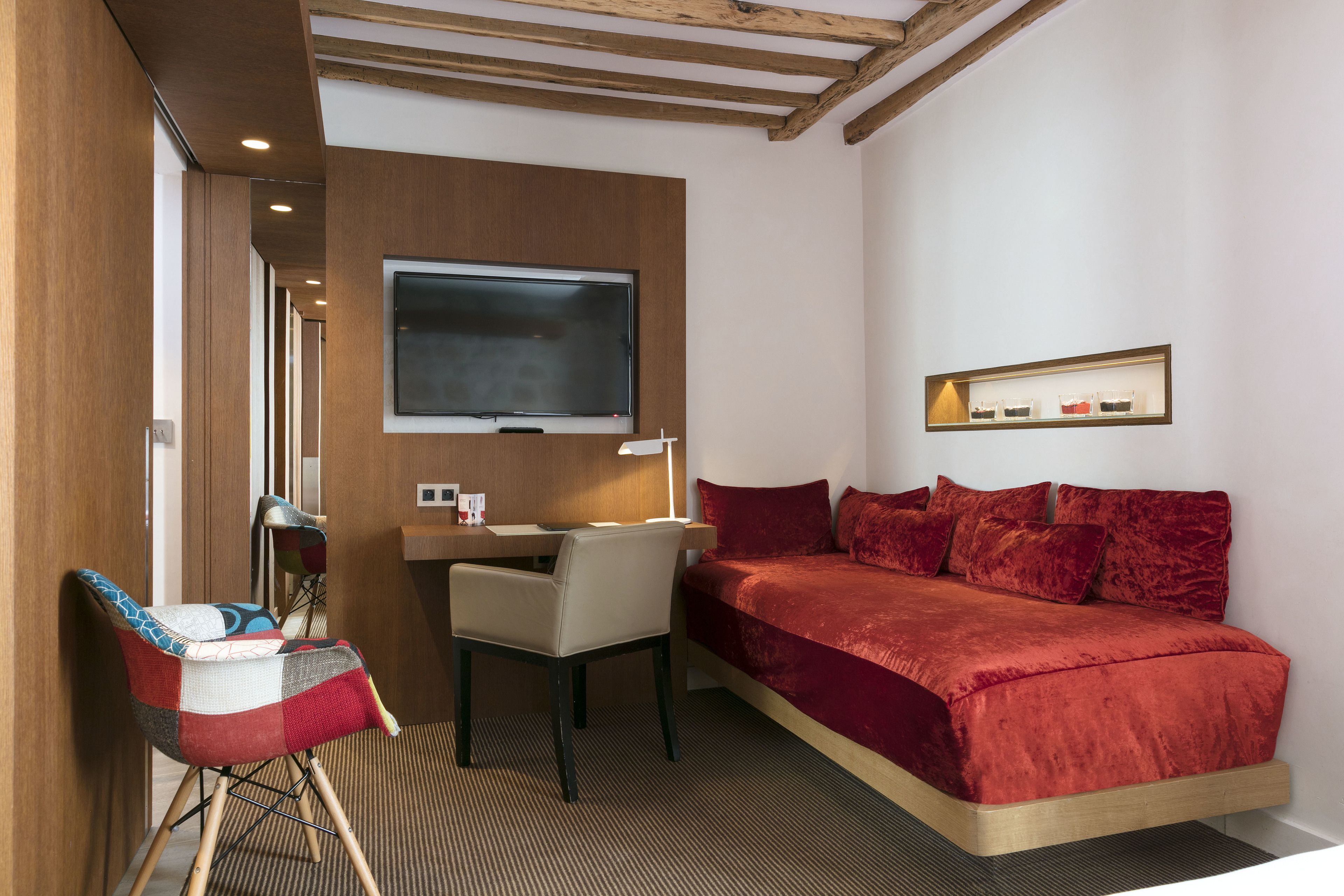 Hotelkamer met een bed, bureau, stoel, televisie en een plank met flessen.
