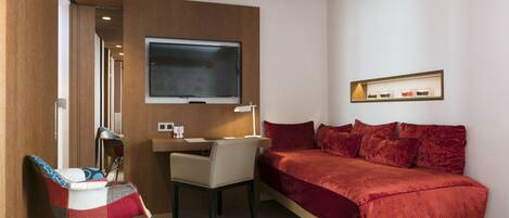 Habitación de hotel con cama, escritorio, silla, televisor y estante con botellas.