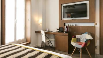 A hotel room with a bed, a desk with a chair, a television, and a coffee machine.