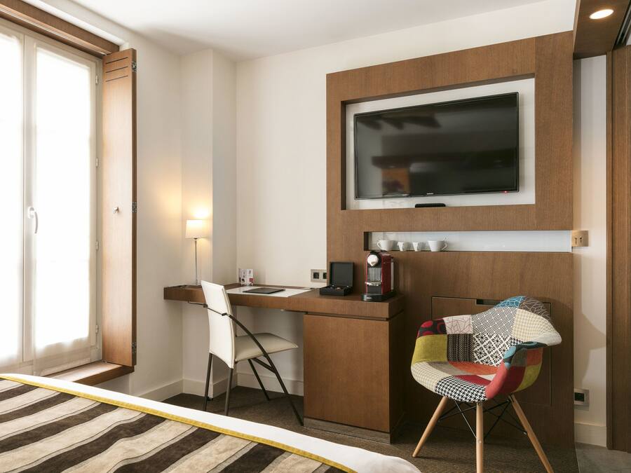 A hotel room with a bed, a desk with a chair, a television, and a coffee machine.