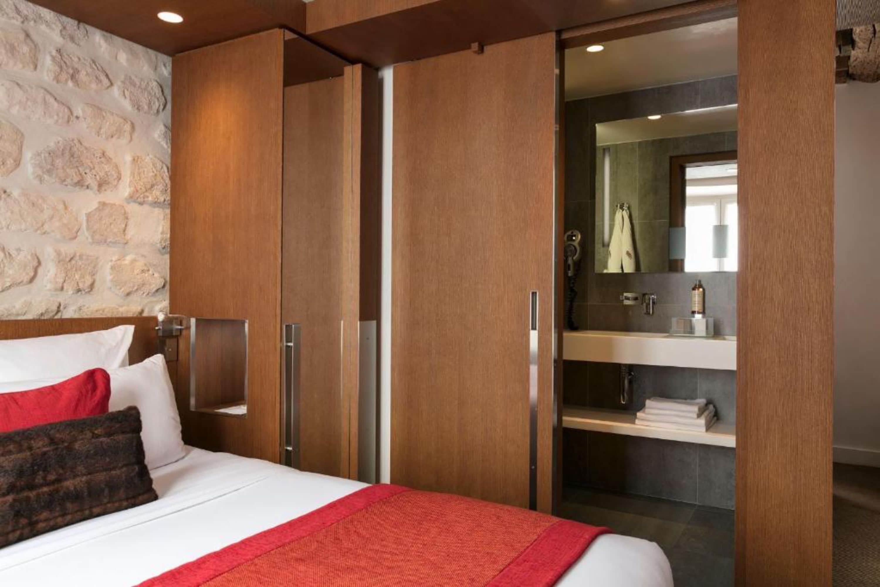 Une chambre d’hôtel comprenant un lit, une armoire en bois et une salle de bain avec un miroir et un porte-serviettes.