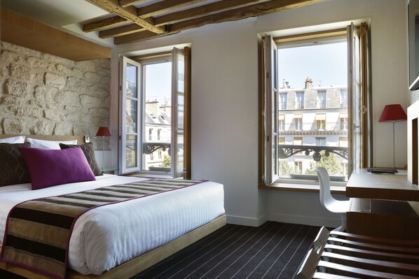 A bedroom with a bed, a desk, and a window with an open shutter.