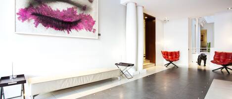 Un vestíbulo amplio con un cuadro abstracto de gran tamaño, un banco y modernas sillas rojas.