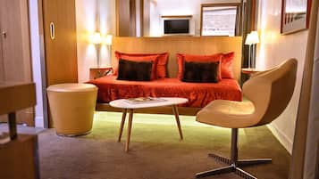 A hotel room with a bed, a chair, a small table, and a trash bin.