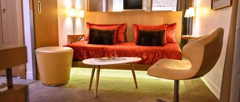 A hotel room with a bed, a chair, a small table, and a trash bin.