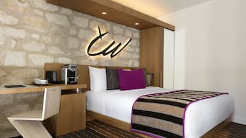 Ett modernt hotellrum med en vägg som har en dekorativ stenbeklädnad, en säng med ett randigt överkast, ett skrivbord med en kaffebryggare och en stol.