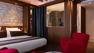 A hotel room with a large bed, a red armchair, a round coffee table, and a stone accent wall.