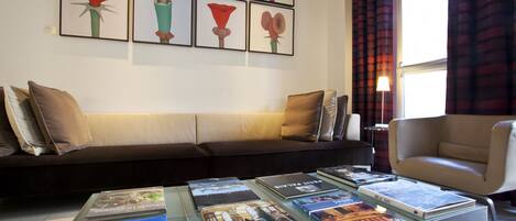 A living room with a sofa, armchairs, a coffee table with books, and a wall with framed artwork.