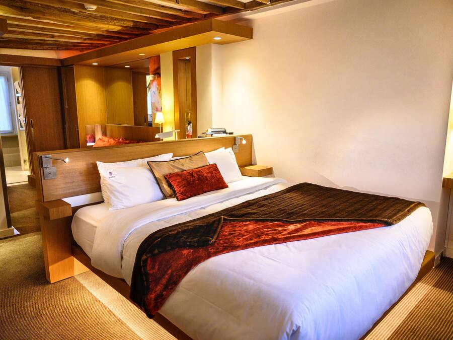 A hotel room with a large bed, wooden headboard, and a mirror above the bed.