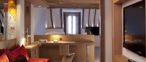 Una habitación de hotel moderna con techo de madera, cama con ropa de cama roja, escritorio con lámpara, televisión y un ventanal grande.