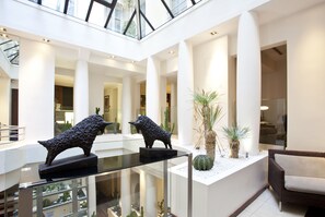 A spacious atrium with high ceilings, a glass ceiling, and a central glass table displaying sculptures. - Select Hotel - Rive Gauche (Paris)