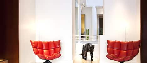 A modern interior with two red leather chairs, a glass partition, and a sculpture of a panther.
