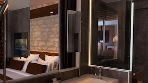 Moderni hotellihuone, jossa on suuri sänky, seinään upotettu televisio, suuri peili ja erillinen kylpyhuone lasiseinäisellä suihkulla.