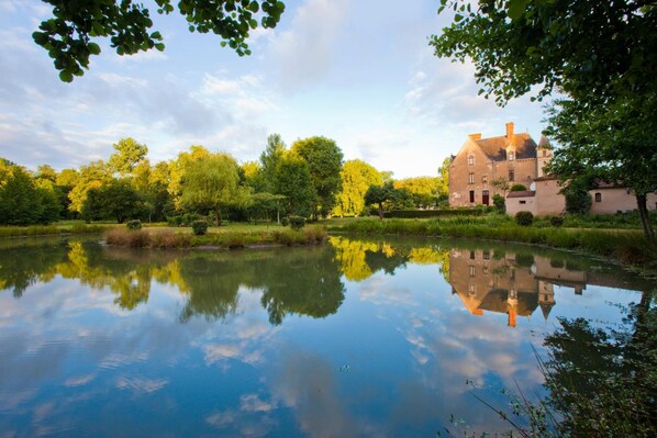 A serene lakeside view with a historic building reflecting in the water, surrounded by lush greenery.