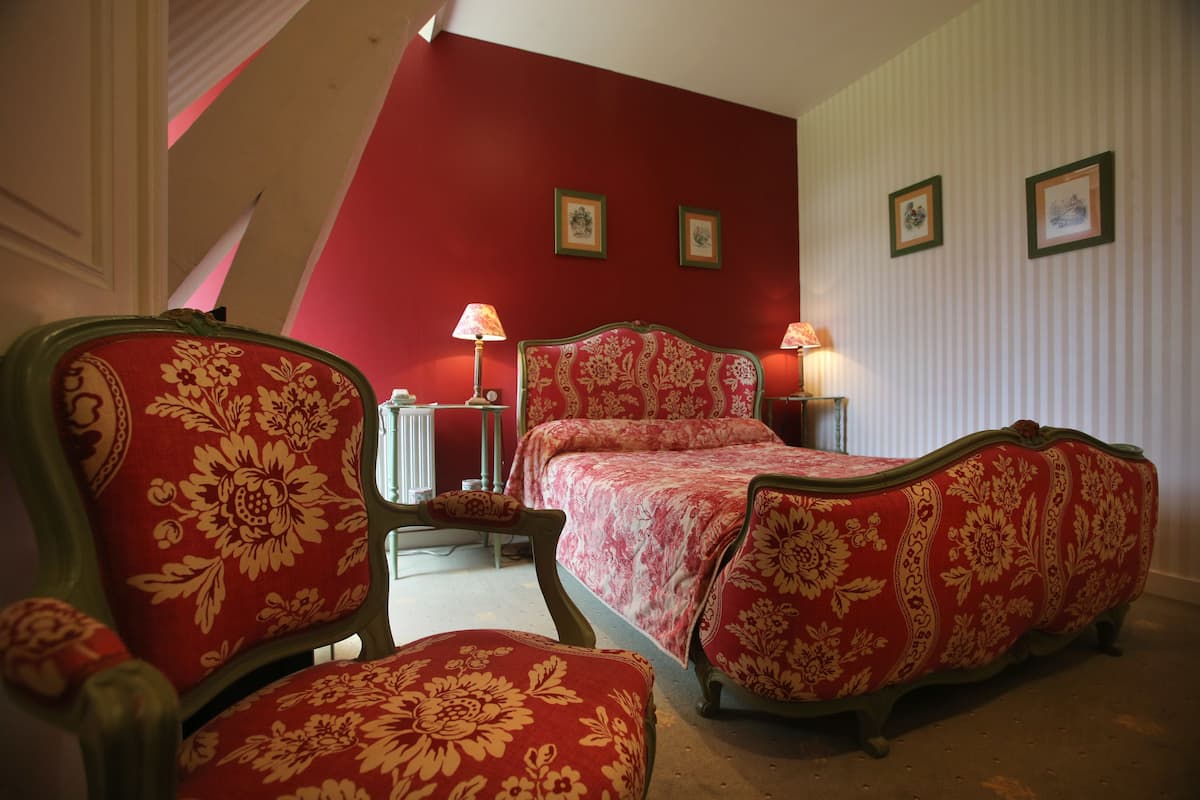 Ein Schlafzimmer mit einer rot-weiß gestreiften Wand, einem Bett mit floralem Bezug, zwei Nachttischlampen und einem Sessel mit floralem Bezug.