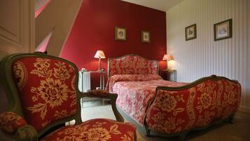 A bedroom with a red and white striped wall, a bed with floral upholstery, two bedside lamps, and a chair with floral upholstery.