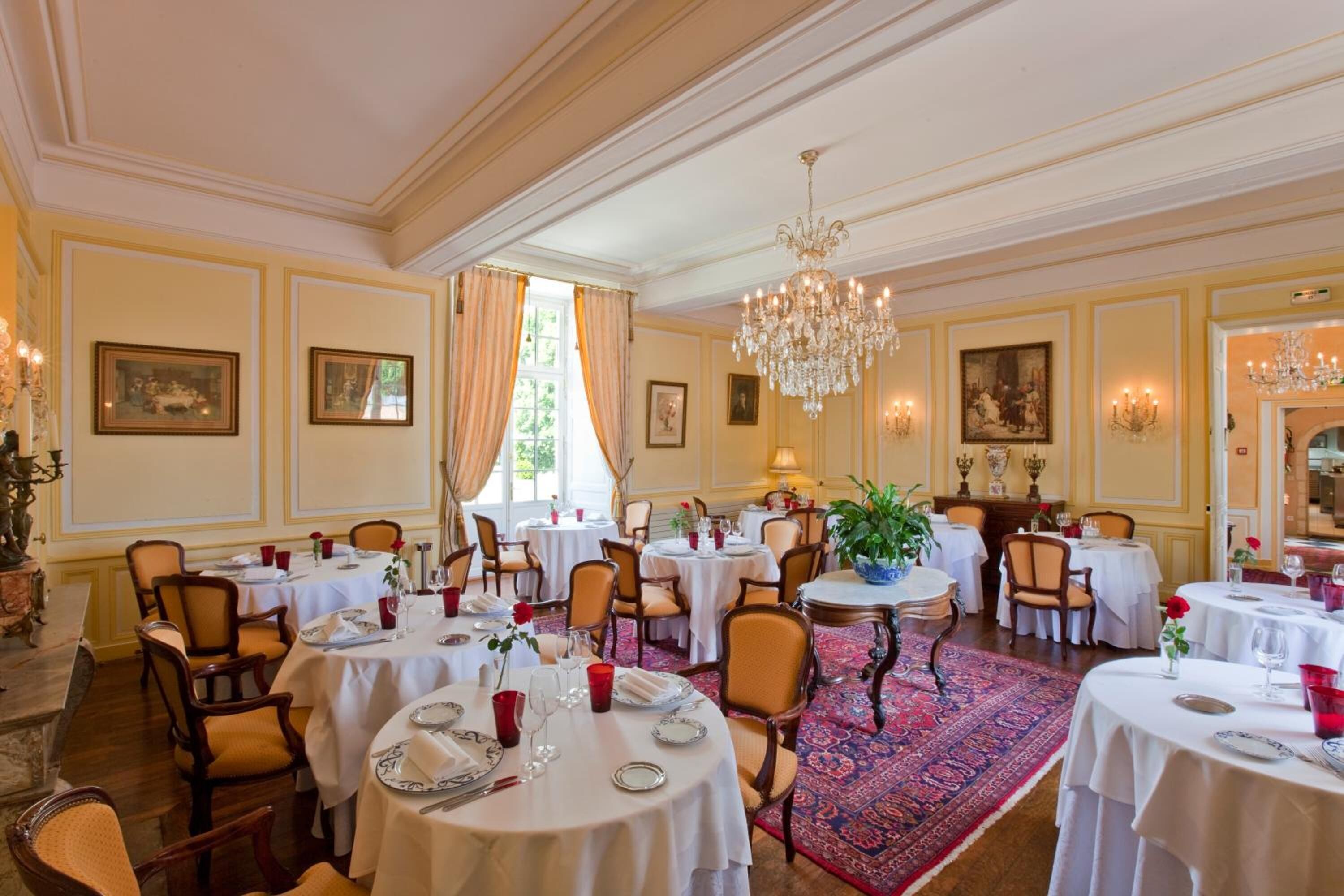 Un comedor formal con varias mesas redondas, sillas y candelabros.