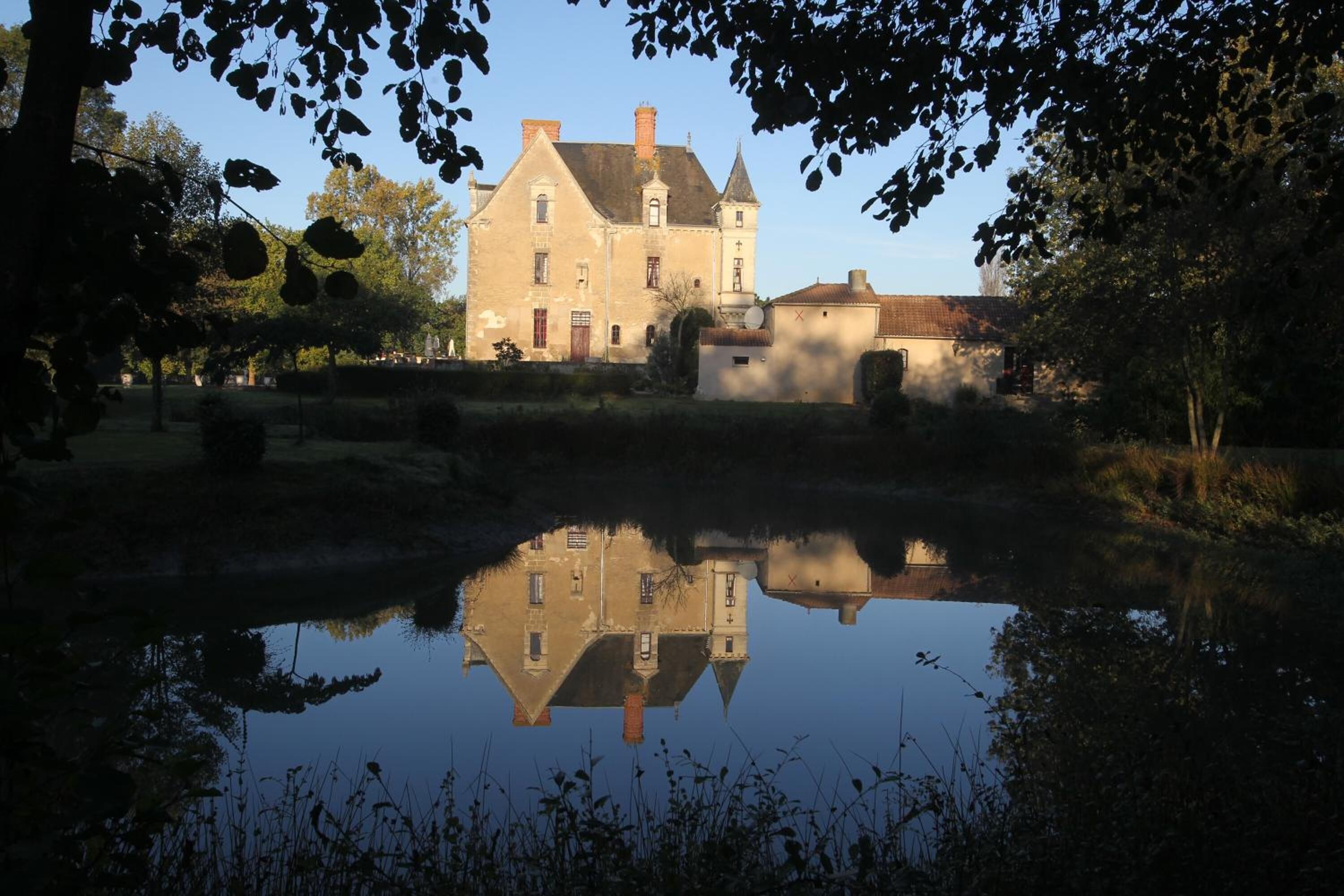 Een historisch gebouw met een weerspiegeling in kalm water, omgeven door bomen en een gazon.