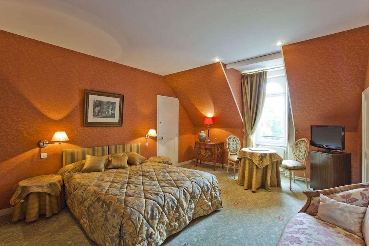 A hotel room with a large bed, a television, a desk with a chair, and a small table with a chair.