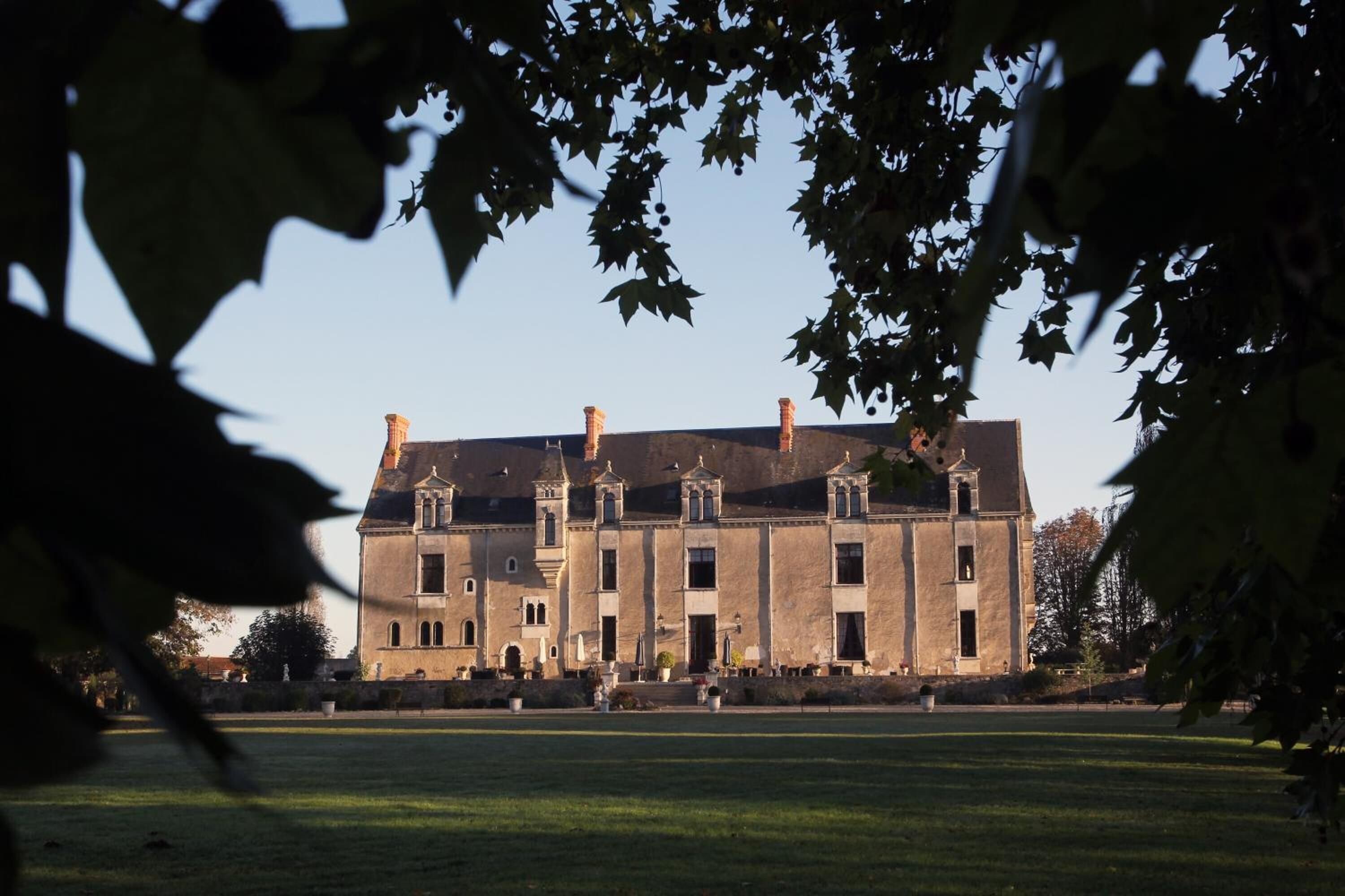 A large, historic building with multiple chimneys and a symmetrical facade, surrounded by a well-maintained lawn.