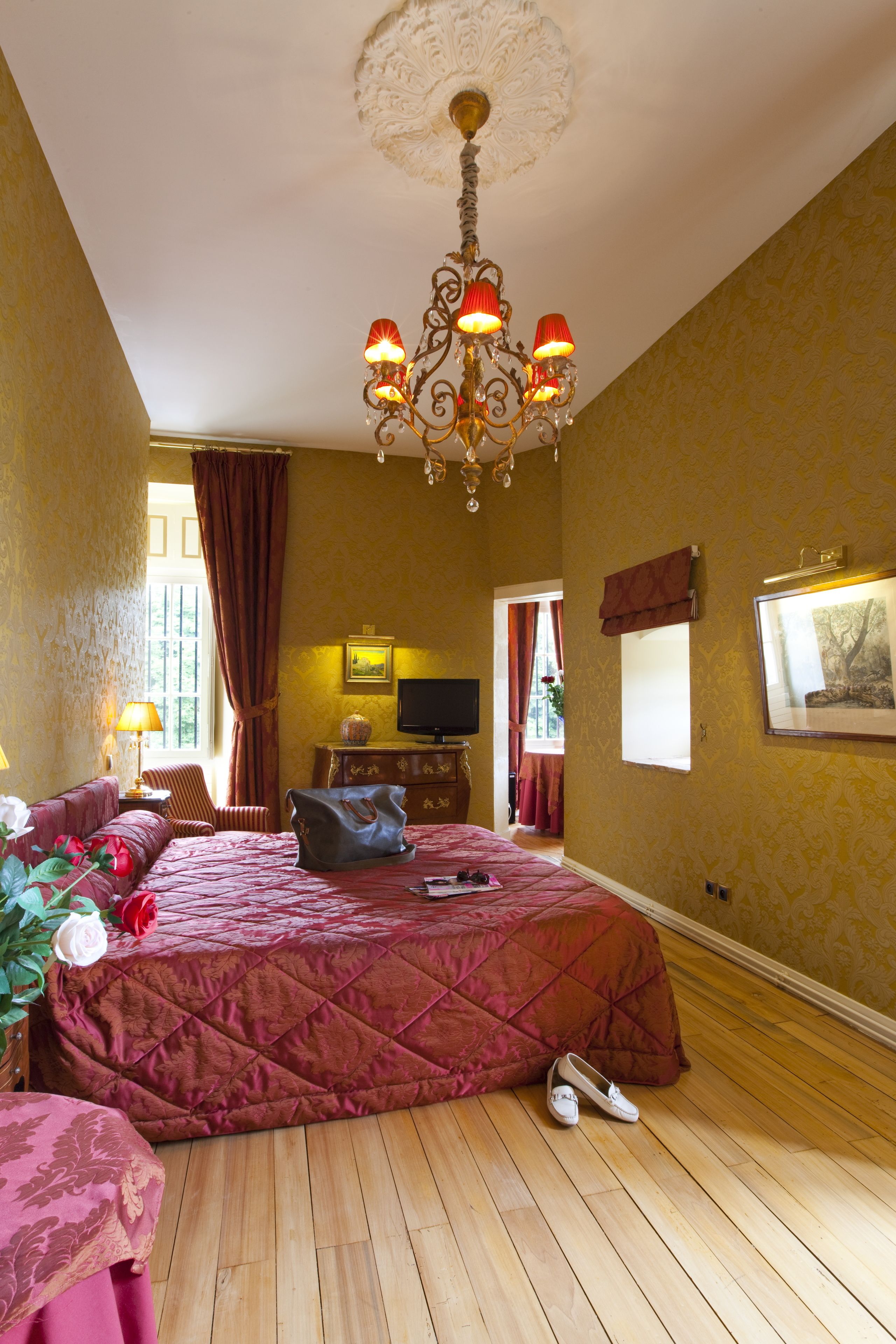 Une chambre d’hôtel avec un grand lit, un lustre, une télévision et une fenêtre avec des rideaux.
