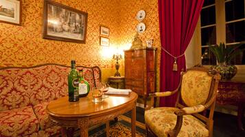 Una habitación con un sofá, una silla de madera, una mesa con una botella y vasos, un armario y una ventana con cortinas.
