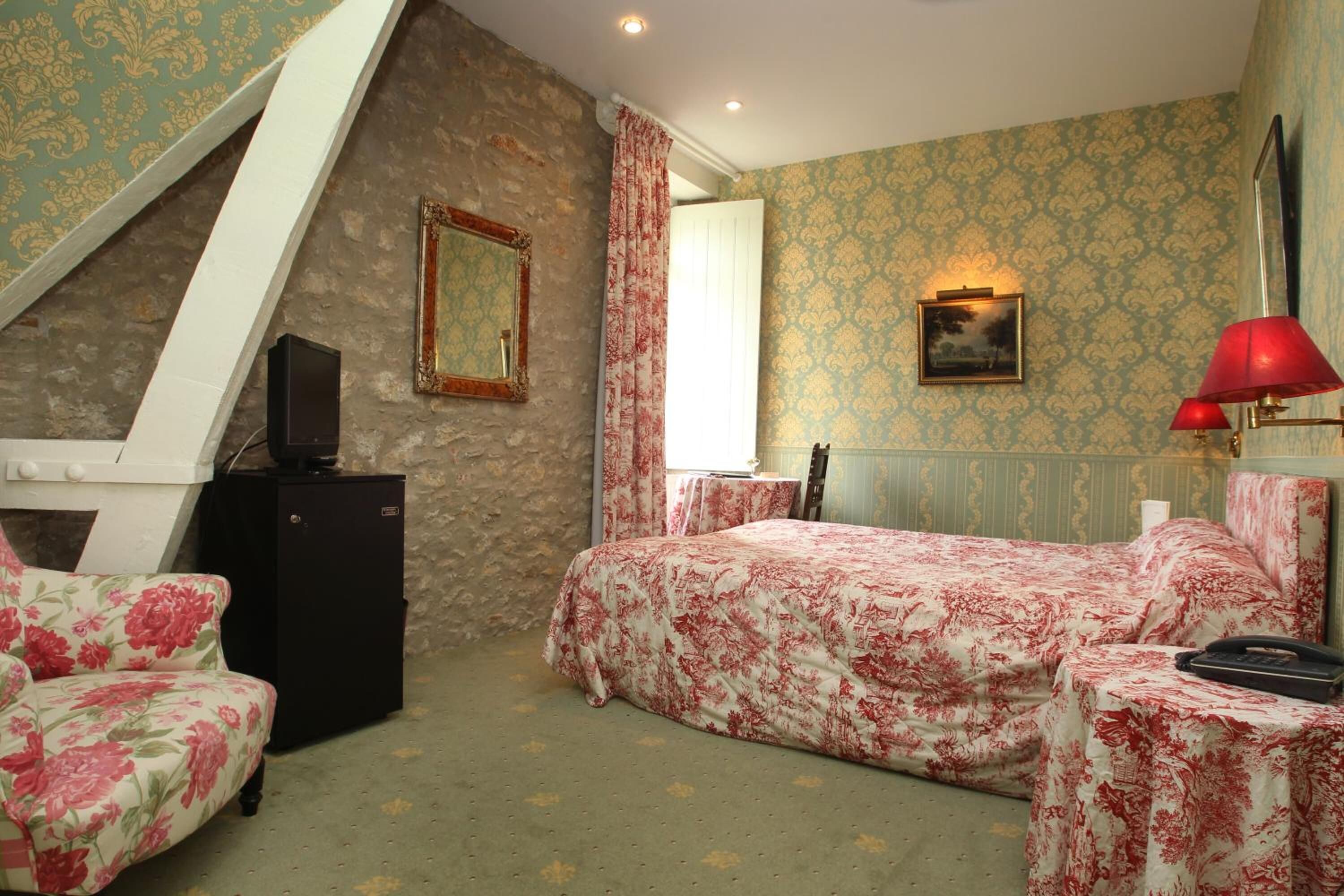 A bedroom with a sloped ceiling, a bed with floral bedding, a desk with a lamp, and a dresser.