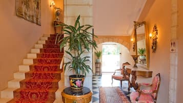 A grand hallway with a checkered floor, a staircase with red carpet, and ornate furniture.