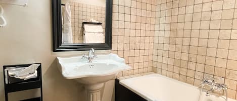 Un baño con un lavamanos blanco de pedestal, un espejo grande, una bañera negra y una pared con azulejos.