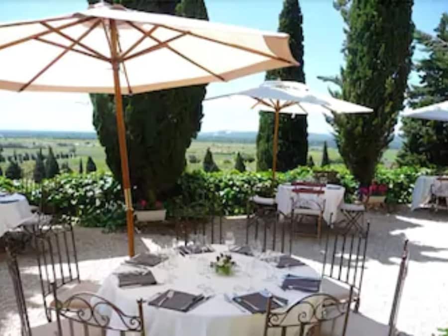 An outdoor dining area with round tables, white tablecloths, and metal chairs.