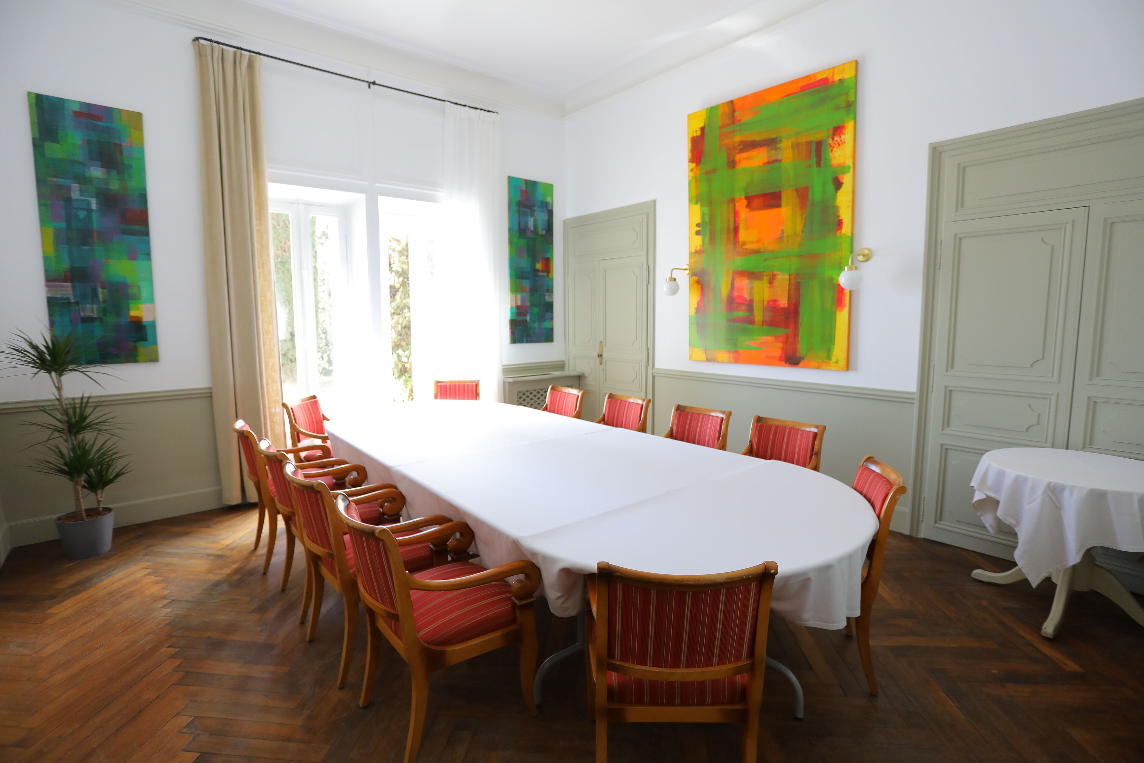 A conference room with a long table, red chairs, and abstract art on the walls.