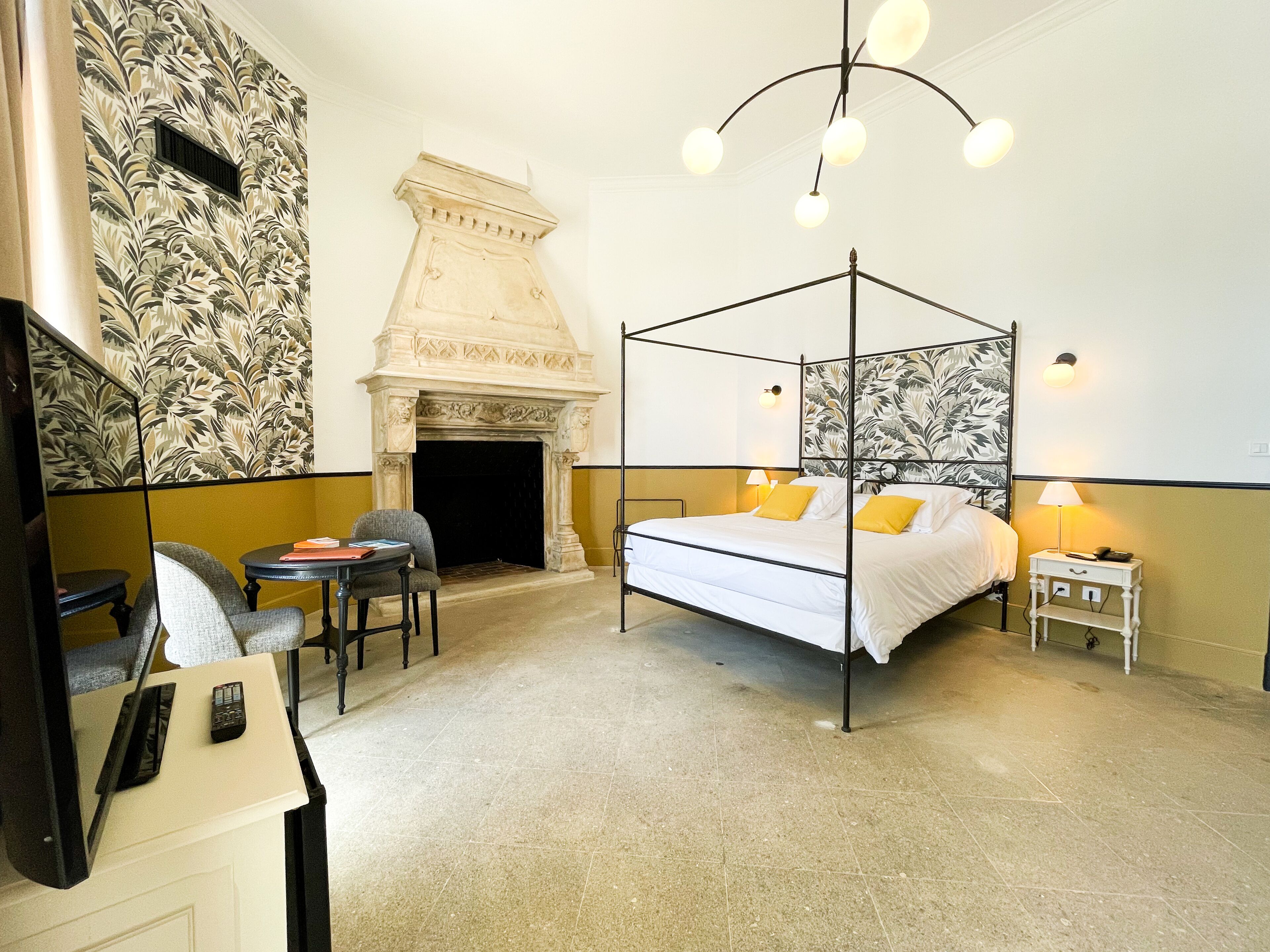 A four-poster bed with a white canopy, a fireplace, a television, and a small table with chairs.