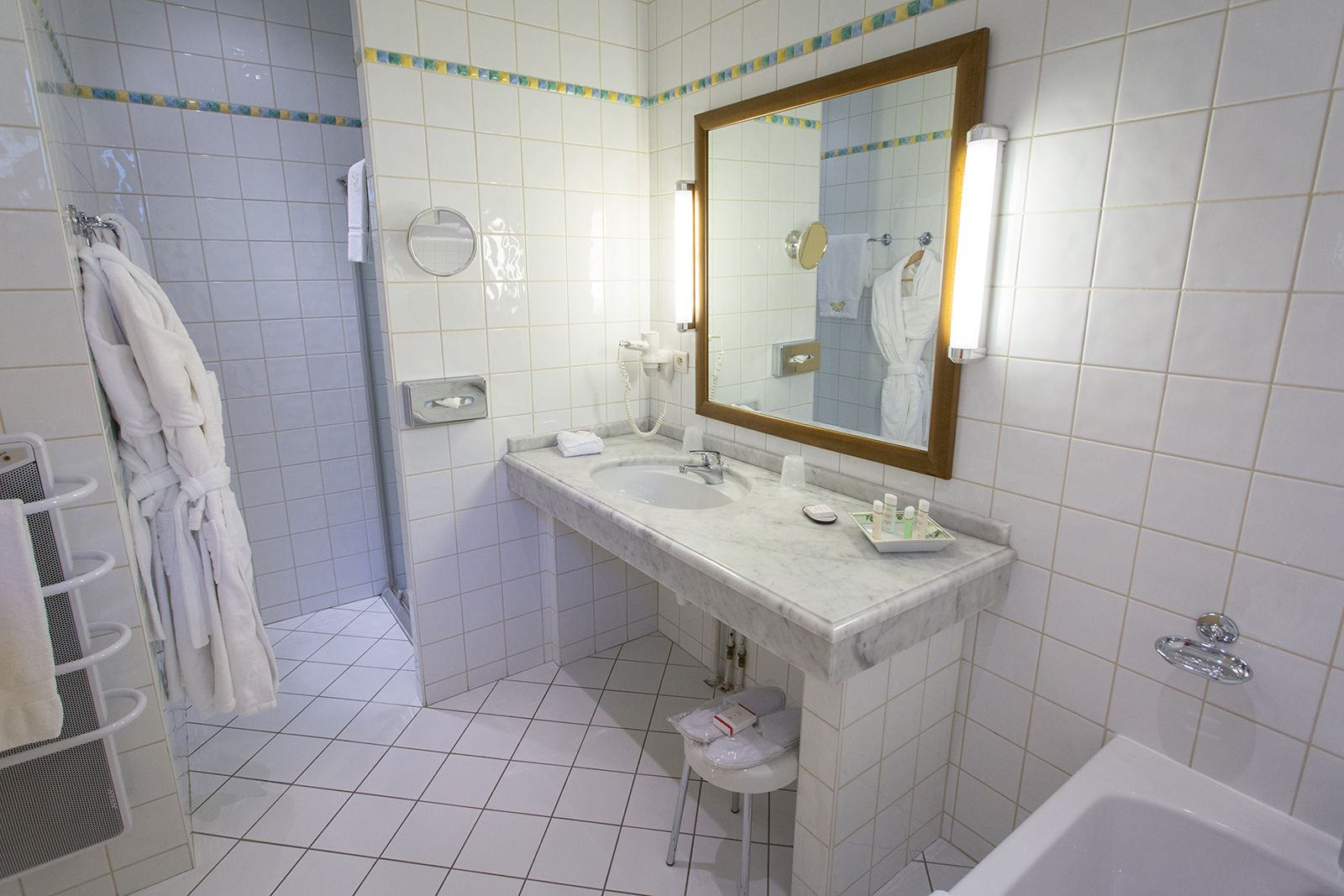 A bathroom with white tiled walls, a marble sink, a large mirror, and a bathtub.
