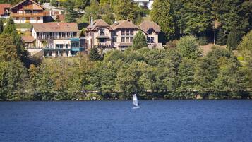 Un lago con un velero, rodeado de casas con balcones y una ladera boscosa.