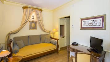 A hotel room with a sofa, a television, a desk, and a lamp.