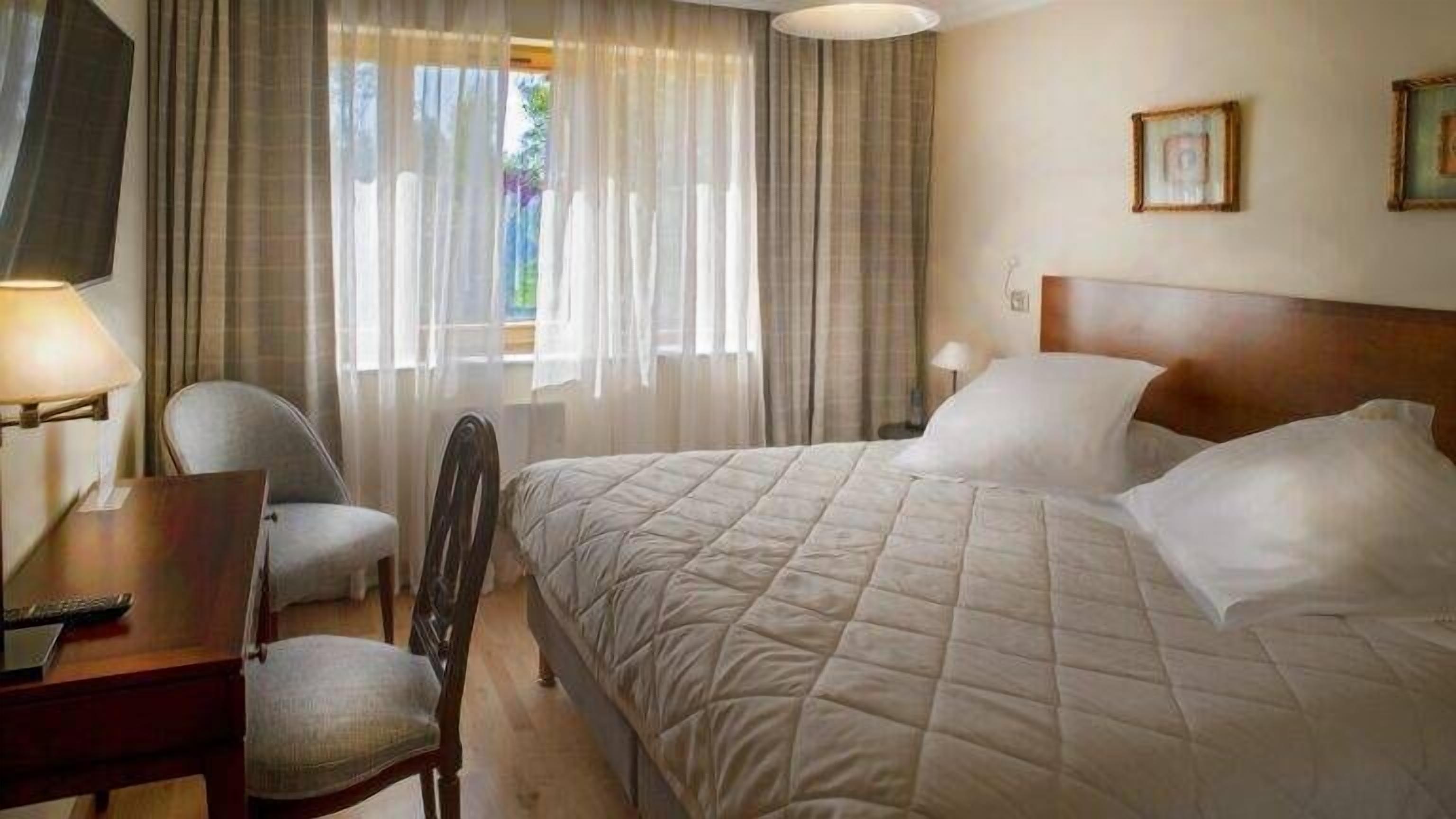 A hotel room with a bed, a desk, a chair, a TV, and curtains.
