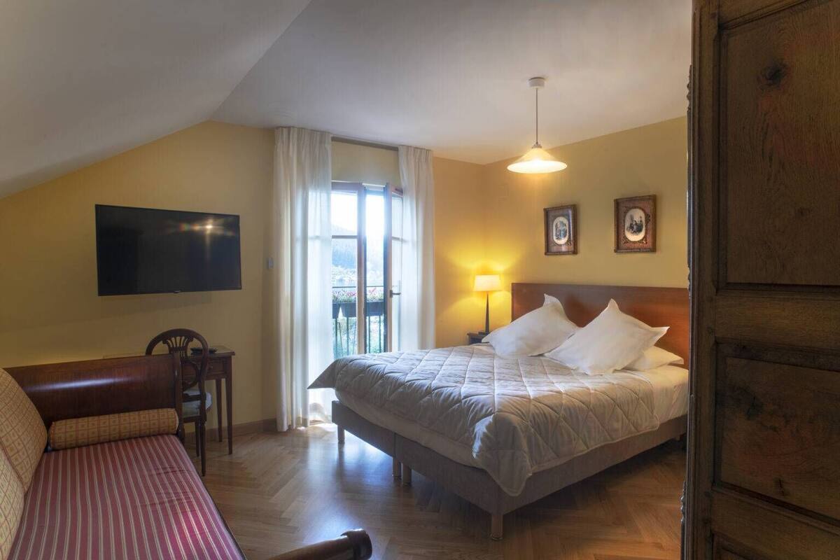 Une chambre d’hôtel avec un lit, un bureau, une chaise, une télévision et un balcon avec des rideaux.