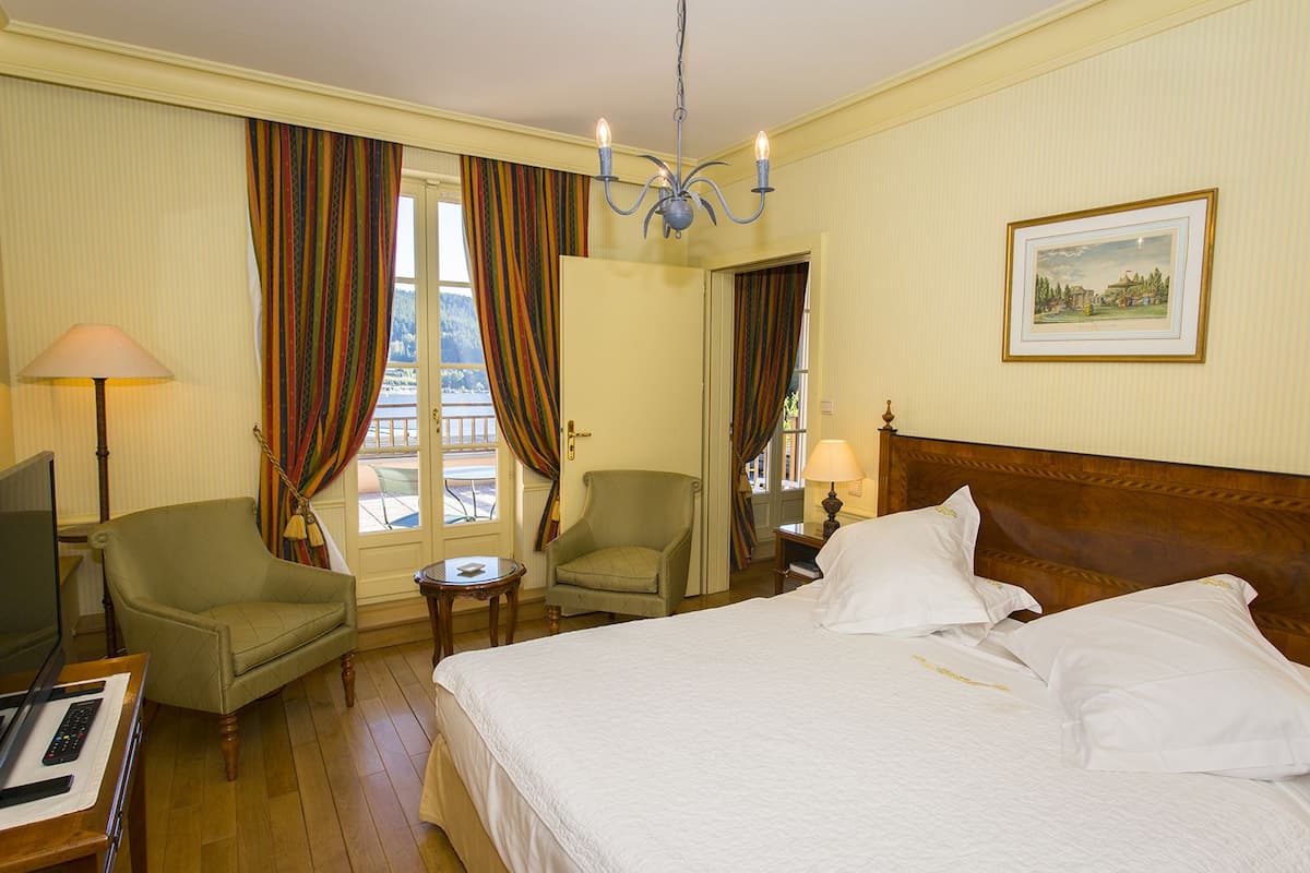 Une chambre d’hôtel avec un lit, deux chaises, un bureau avec un ordinateur, une lampe et un tableau au mur.