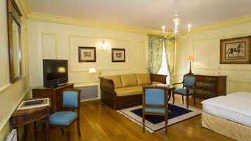 Quarto de hotel com televisão, sofá, duas poltronas, cama, cômoda e lustre.