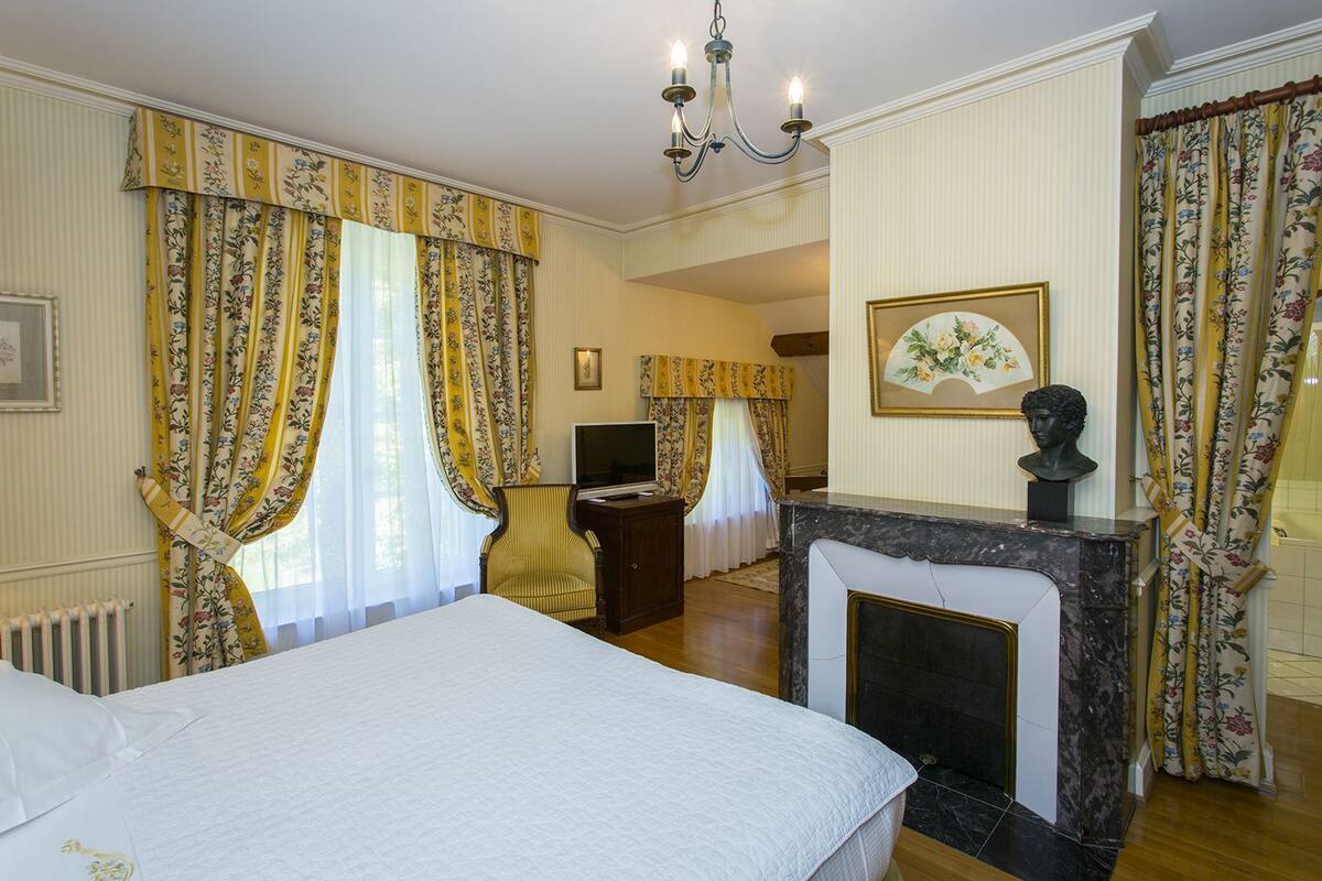 Une chambre d’hôtel avec un lit, une télévision, une cheminée et des rideaux à motifs floraux.