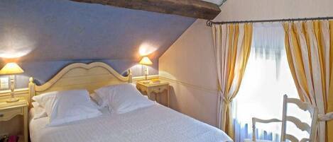 A bedroom with a bed, two bedside lamps, a chair, and a window with curtains.