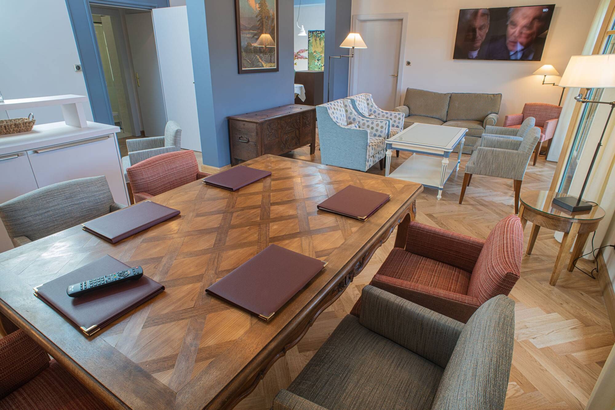 Un vaste espace de vie comprenant une table à manger en bois, plusieurs fauteuils rembourrés, un canapé et un téléviseur fixé au mur.