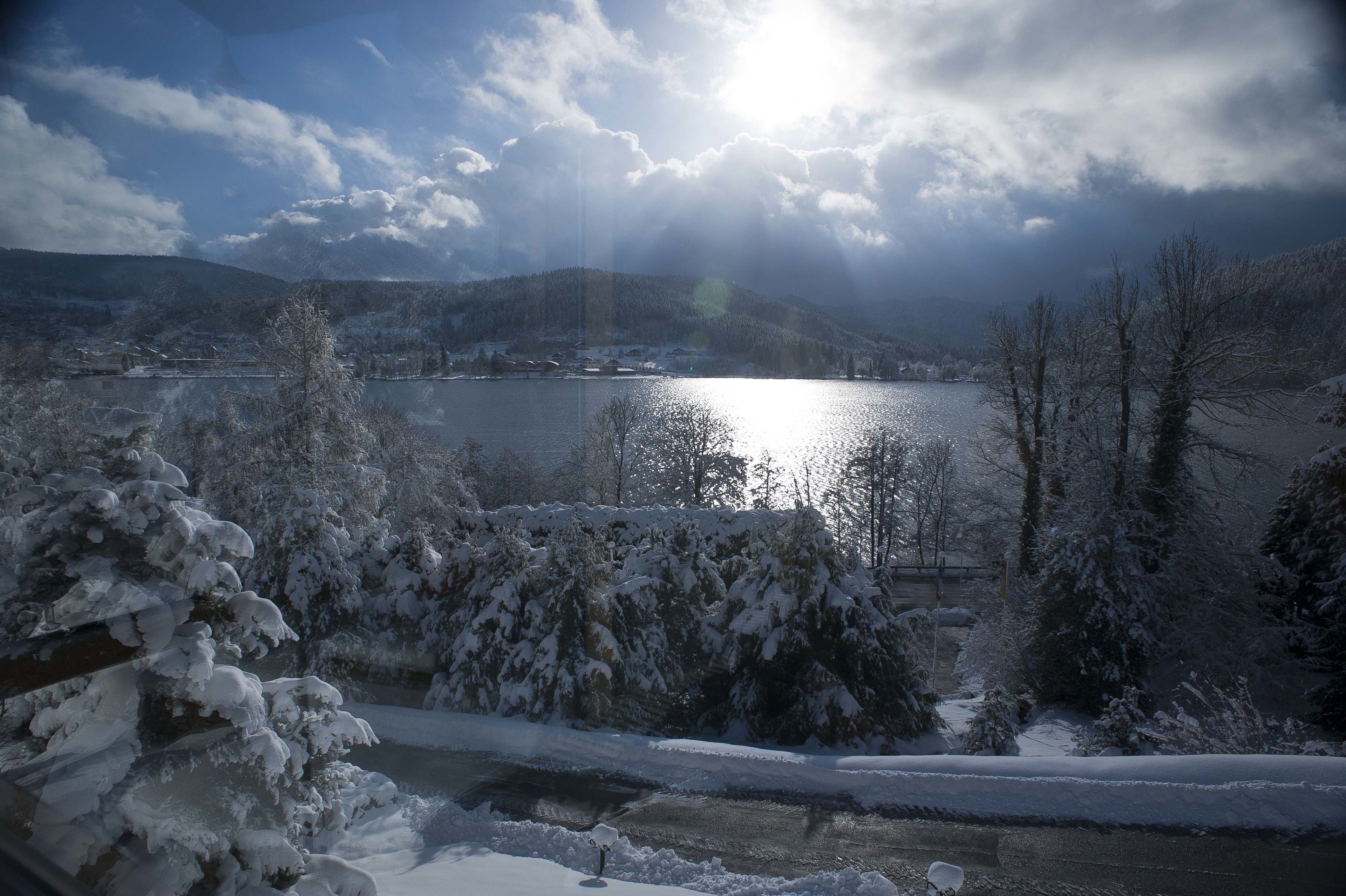 Paisatge hivernal amb un llac, arbres coberts de neu i un cel clar.