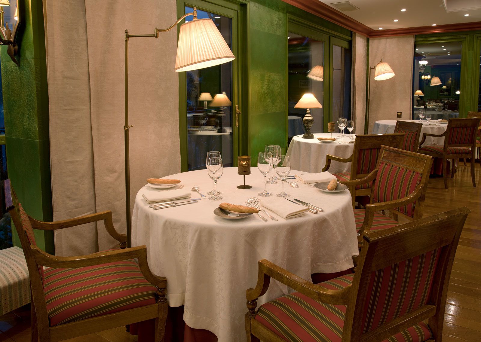 Un espace repas avec des tables rondes, des chaises et une décoration de table comprenant des assiettes, des verres et des couverts.